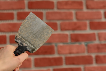 The master's hand is holding putty knife patchingwith traces of concrete mortar on the background...