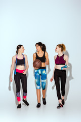 happy african american girl holding basketball and walking with sportive women on white