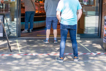 Tape put on floor to ensure people are distanced from each other. Social distancing of people waiting in line queue in front of food store due to limit for customers in store during covid-19 outbreak