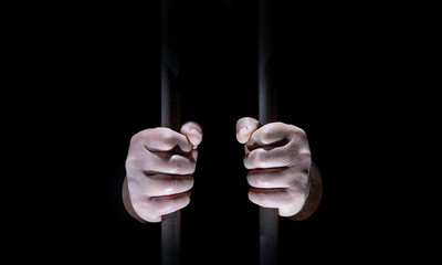 A man is in a prison. His fists cling to the bars.