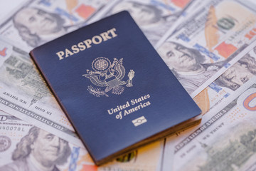 One single blue American passport on top of a pile of US dollars