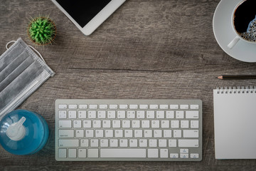 work from home concept, tablet keyboard on vintage wooden office desk table with surgical face mask, alcohol gel