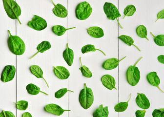 Fresh green spinach leaves pattern over white wooden table background. Vegan food trend. Eco-conscious concept. Top view.