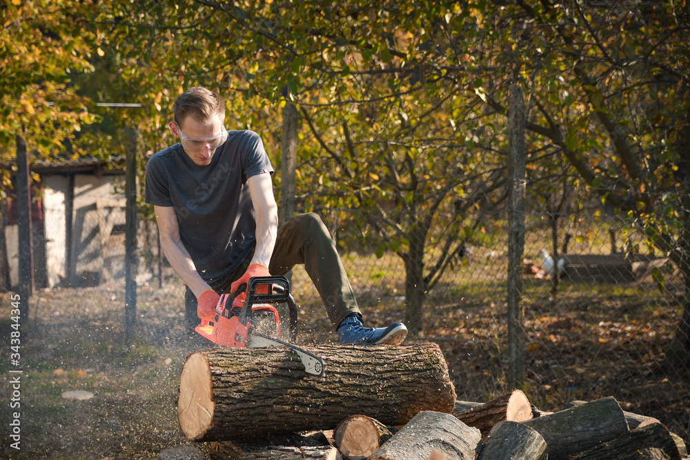 Poster chainsaw that stands on a heap of firewood in the yard on a beautiful background of green grass and 