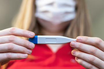 Closeup photo of woman looking at digital thermometer. Concept of illness, fever. Selective focus, blurred background.