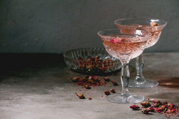 Crystal vintage glasses of pink rose champagne, cider or lemonade with dry rose buds. Grey texture background.