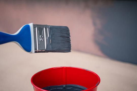 Paint Brush And A Bucket With Paint Next To A Building Exterior Wall. Painting House Plinth Outside. Home Renovation. Nobody
