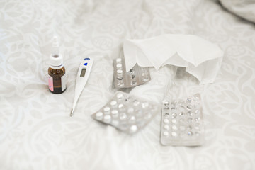 medicines with a thermometer lying on the bed