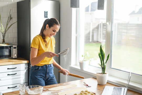 Learn cooking online. A young woman is watching cooking tutorial video in the kitchen and sift a flour, she is going to bake