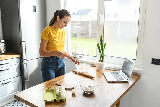 Cook at home. A young woman in casual clothes in the kitchen is going to bake a cake, cookies, she is sifting flour on the table