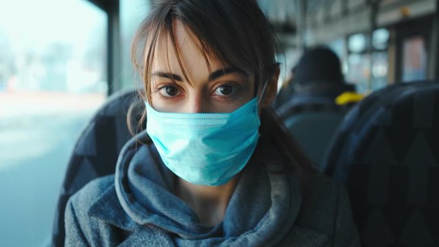 attractive confident mixed rase young woman in protective medical mask looking straight at camera while sitting in city public transport