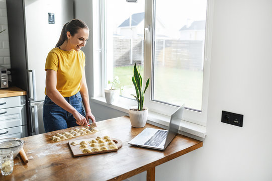 A young woman learns to cook, she watches video recipes on a laptop in the kitchen and cook a dish from the dough. Cooking at home concept