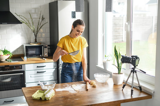 Food vlogs. A young woman makes cooking videos in the kitchen. She sifts the flour on the table and looks at the camera with a smile