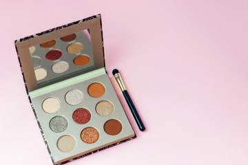 Multi-colored pastel brown red eye shadow on a pink background with brushes.