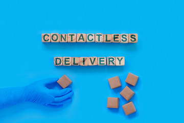 Cardboard boxes with groceries or other purchases on a blue background. Hand in a medical glove with box. The inscription on wooden cubes 