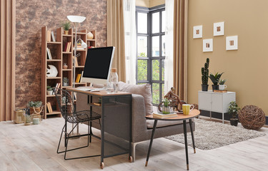 Brown living room interior decoration with wallpaper detail, grey sofa, wooden coffee table and working desk in the living room.