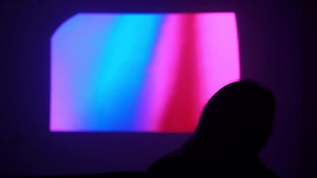 Silhouette of a girl on the background of the screen on the wall. Woman is watching a movie on a projector. What to do at home. Watching a movie at home. Stay home. Have fun at home. Quarantine. 