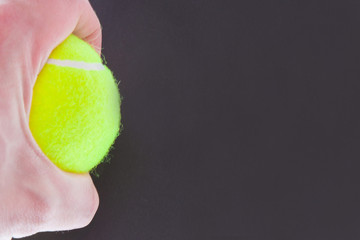 Tennis ball and man's hand on the black background