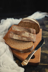 whole grain  bread lies on a wooden board on a black wooden background
