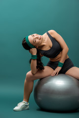 Attractive asian sportswoman smiling and looking up on fitness ball on green