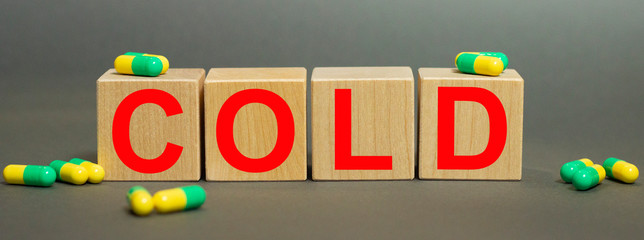The common cold is written on wooden cubes with capsules on a gray background. Virus. Pandemic. Self-isolation.