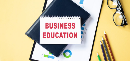 glasses, coffee mug and notebook with BUSINESS EDUCATION word on wooden table. business conceptual