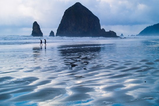 The  waves at low tide and the Haystack rocks at Cannon beach with beautiful reflections with cloudy sky.