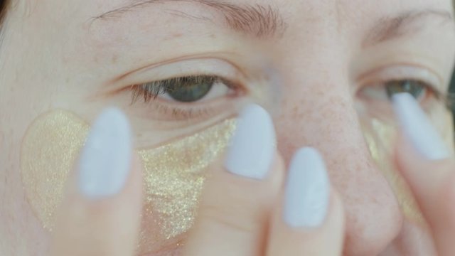 Woman imposes patches under the eyes of a refreshing mask. Woman with collagen pads under her eyes. Cosmetic procedures. At home. Close-up