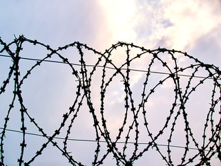 barbed wire against the background of clouds through which sunlight breaks through, the concept of freedom, unfreedom, close-up
