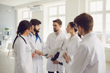 Group of practicing doctors in a meeting discuss the diagnosis of a patient standing in a clinic office.