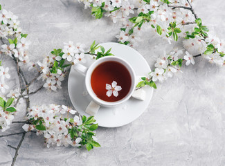 A white Cup of tea on the table and blooming branches of a fruit tree flat lay top view