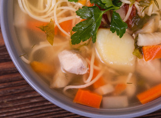Chicken broth soup with noodles, vegetables and parsley on a wooden table, macro photography