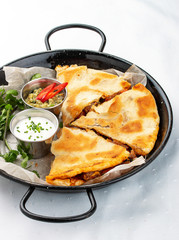 Quesadilla in a pan with guacamole and cream sauce. Traditional mexican dish. On light background