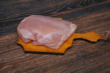 Ingredient for cooking. Raw turkey lies on a wooden board on a dark kitchen table. Filet of the bird is ready for cutting with a knife.