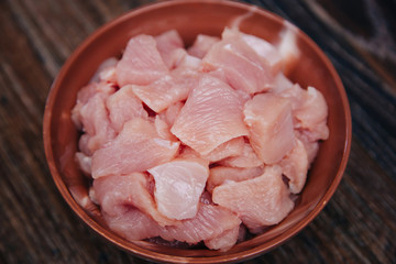 Ingredient for cooking. Raw turkey diced in a black cup on a dark kitchen table. Fillet cut into pieces. Chicken meat