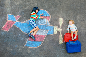 Obraz premium Two little children, kid boy and toddler girl having fun with with airplane picture drawing with colorful chalks on asphalt. Siblings painting with chalk and going on vacations.