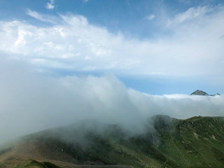 High mountains with green slopes, wrapped in dense fog. Dense fog in the mountains on a sunny, bright day. Krasnaya polyana, Russia.