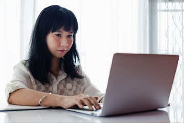 Asian woman using laptop and working at home for business, self-quarantine, staying home and social distancing in coronavirus or Covid-2019 outbreak situation concept