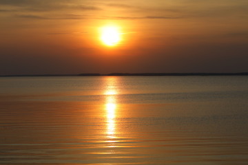 Orange sunset.The hot ball of the sun in the clear sky and the reflected Golden path on the smooth...