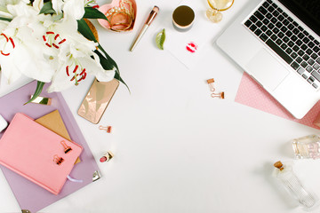 Creative colorful female workspace with laptop computer, flowers, colorful notebooks, golden clips on white desk. Flat lay, top view