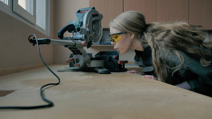 Girl with protective glasses blows sawdust off the table