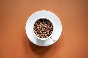 Top view of roasted coffee beans in white coffee cup with brown background 