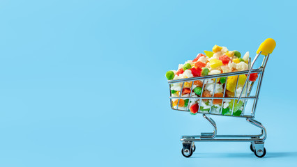 Frozen vegetables assorted in toy shopping cart on blue background. Full of assorted frozen vegetables food shop trolley. Banner with copy space left