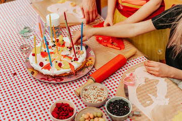 Children preparing homemade birthday cake with candles and colorful topping.
