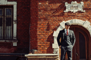 Portrait of retro 1920s english arabian business man wearing dark suit, tie and flat cap standing...