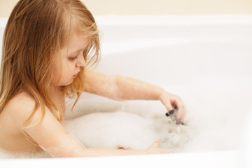 Obraz premium little baby girl with blond hair playing with foam in a bath tub. girl takes a bath. girl playing with toys in the bath
