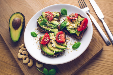 Avocado sandwich with tomatoes, basil, garlic and cashew nuts. White plate and wooden background. Close, blue shadows.