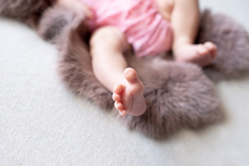 Feet of the newborn baby. pink color. mother's day. little girl in pink bodysuit lies on brown rabbit fur