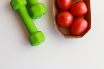 green dumbbells and krvsny tomatoes on a white background. lose weight by summer on quarantine
