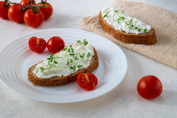 Fototapeta na wymiar Sandwich on whole grain bread with homemade cream cheese or cottage cheese, microgreens and cherry tomatoes. Healthy food, balanced food concept. Horizontal orientation, selective focus.